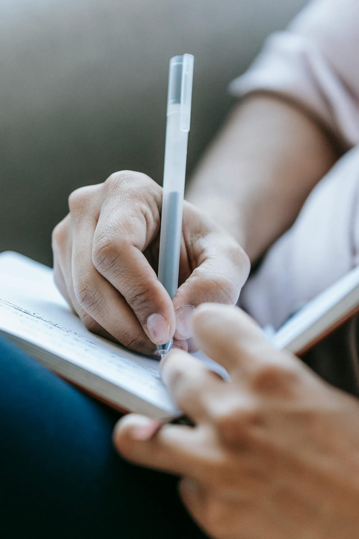 Mano sosteniendo un bolígrafo y escribiendo en un cuaderno abierto.