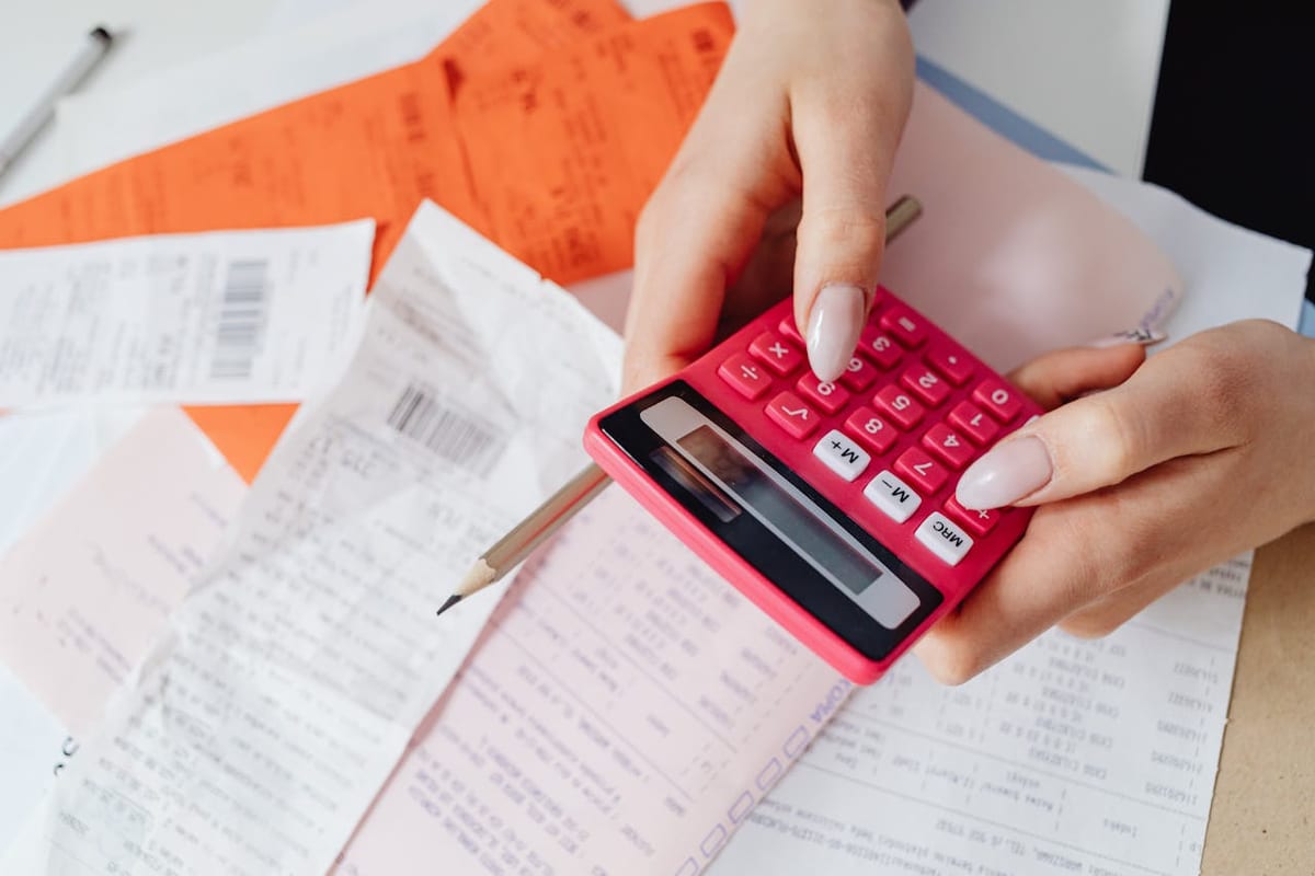 Manos usando una calculadora rosada sobre recibos de papel apilados.